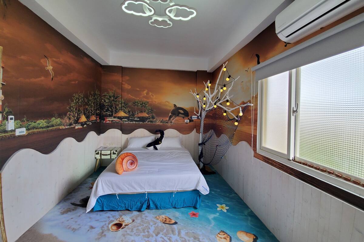 A bedroom with a bed, a mural on the wall, a ceiling light fixture, and a window with blinds.