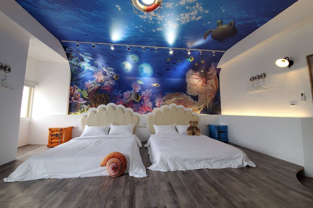A bedroom with two beds, a mural of an underwater scene, a ceiling light, and a wall-mounted heater.
