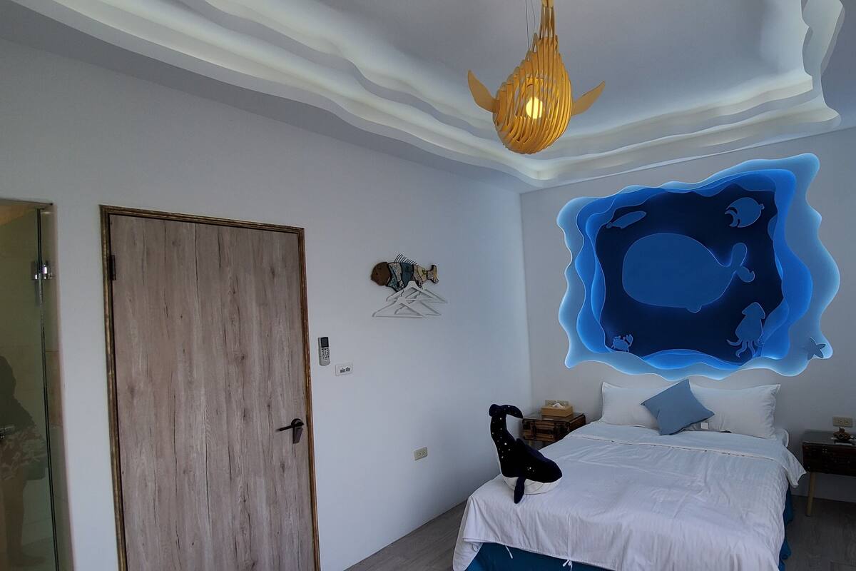 A bedroom with a bed, bedside table, and a wall decoration.
