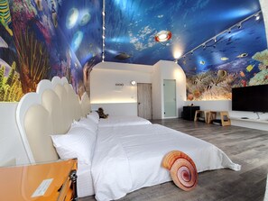 A bedroom with a large bed, a TV, and an aquarium wall.