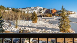 A hotel with a ski slope in the background, a parking area with several vehicles, and a clear blue sky. - ⭐️ 2 Level Unit w/ Pool ⎮Hot Tubs ⎮Private Deck (Steamboat Springs)