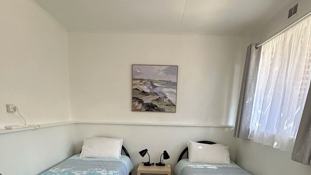 Ett rum med två separata sängar, ett litet sängbord, en tavla som hänger på väggen och ett fönster med gardiner.