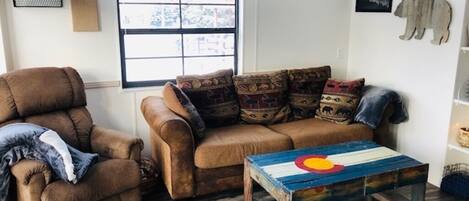 A living room with a brown sofa, a brown armchair, and a wooden coffee table with a colorful design.