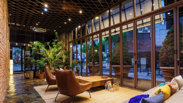 A modern indoor seating area with a brick wall, large windows, and potted plants. - LACOZi STAY Seoul (Seoul)