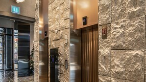 A modern elevator area with stone walls, a metallic elevator, and a clear floor path. - LACOZi STAY Seoul (Seoul)