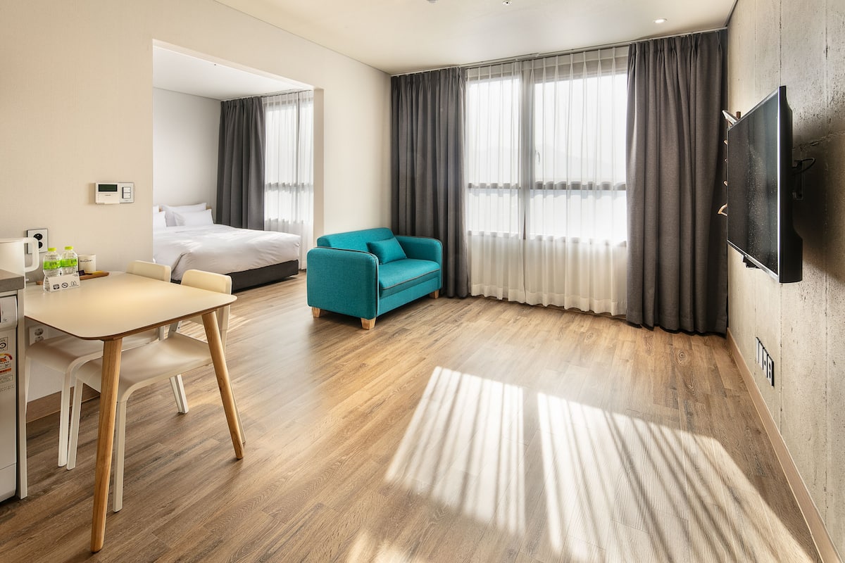 Una camera d'albergo con un letto, una poltrona, una televisione, una scrivania con una sedia e un pavimento in legno.