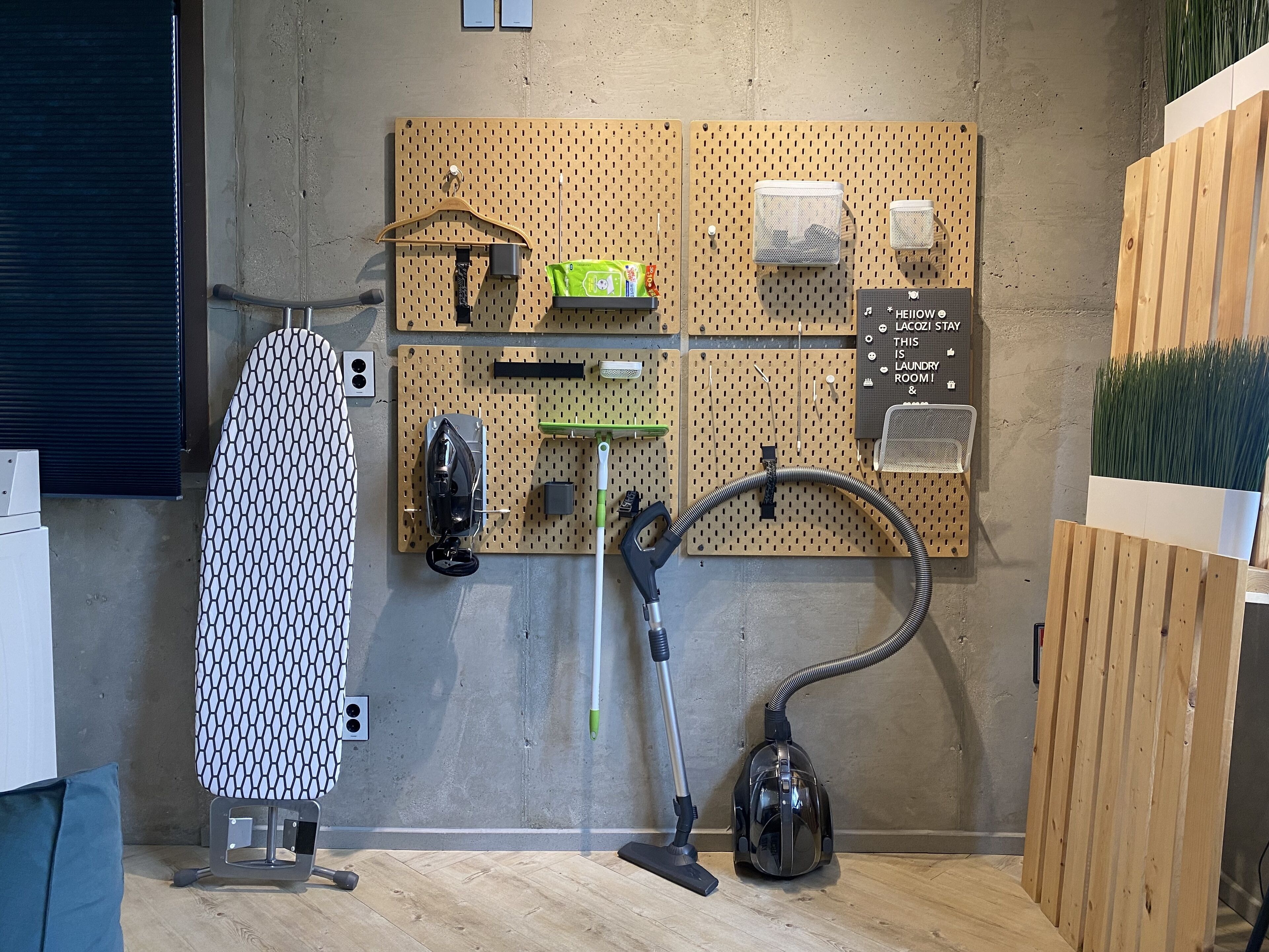 A laundry room with a wall-mounted ironing board, a vacuum cleaner, and a pegboard with various items.