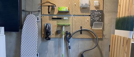 A laundry room with a wall-mounted ironing board, a vacuum cleaner, and a pegboard with various items.