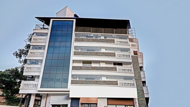 A multi-story building with a central glass facade, balconies, and a mix of stone and concrete exterior. - Itsy Hotels Dew Dreams (Aluva)