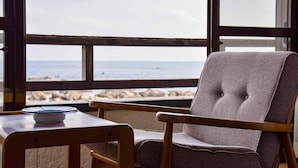 A chair with a woven backrest and a wooden table with a blue object on it, positioned near a window with a view of the sea. - Misaki Kanko Hotel (Muroto)