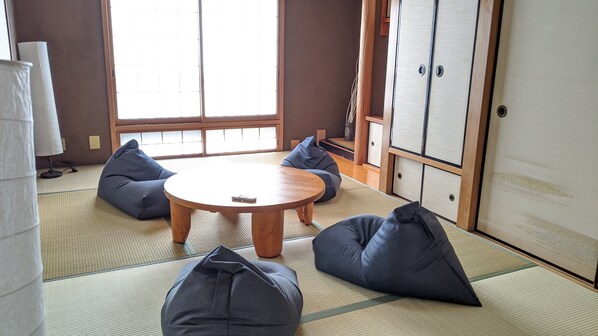 A tatami mat room with a round wooden table, four bean bags, and sliding doors.