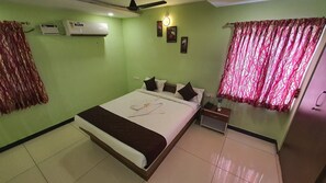 A neatly arranged hotel room with a bed, bedside table, and an air conditioning unit on the wall. - JR Stays (Coimbatore)