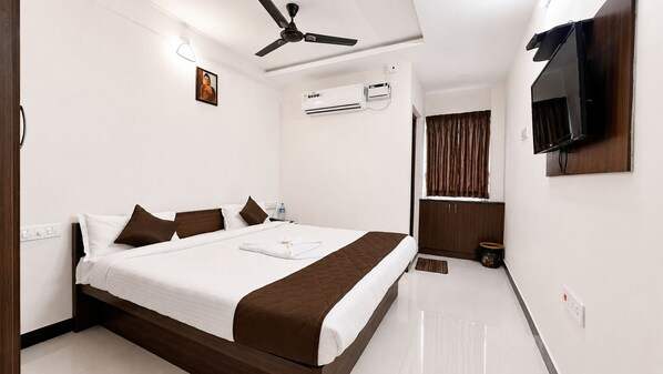 A hotel room with a bed, a ceiling fan, an air conditioning unit, a television, and a window with curtains.