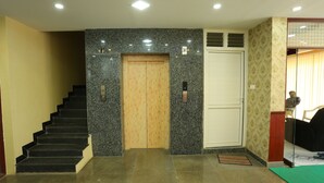 A hotel lobby with a staircase, a wooden elevator, a white door, and a patterned wall. - JR Stays (Coimbatore)