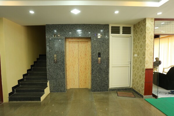 A hotel lobby with a staircase, a wooden elevator, a white door, and a patterned wall. - JR Stays (Coimbatore)