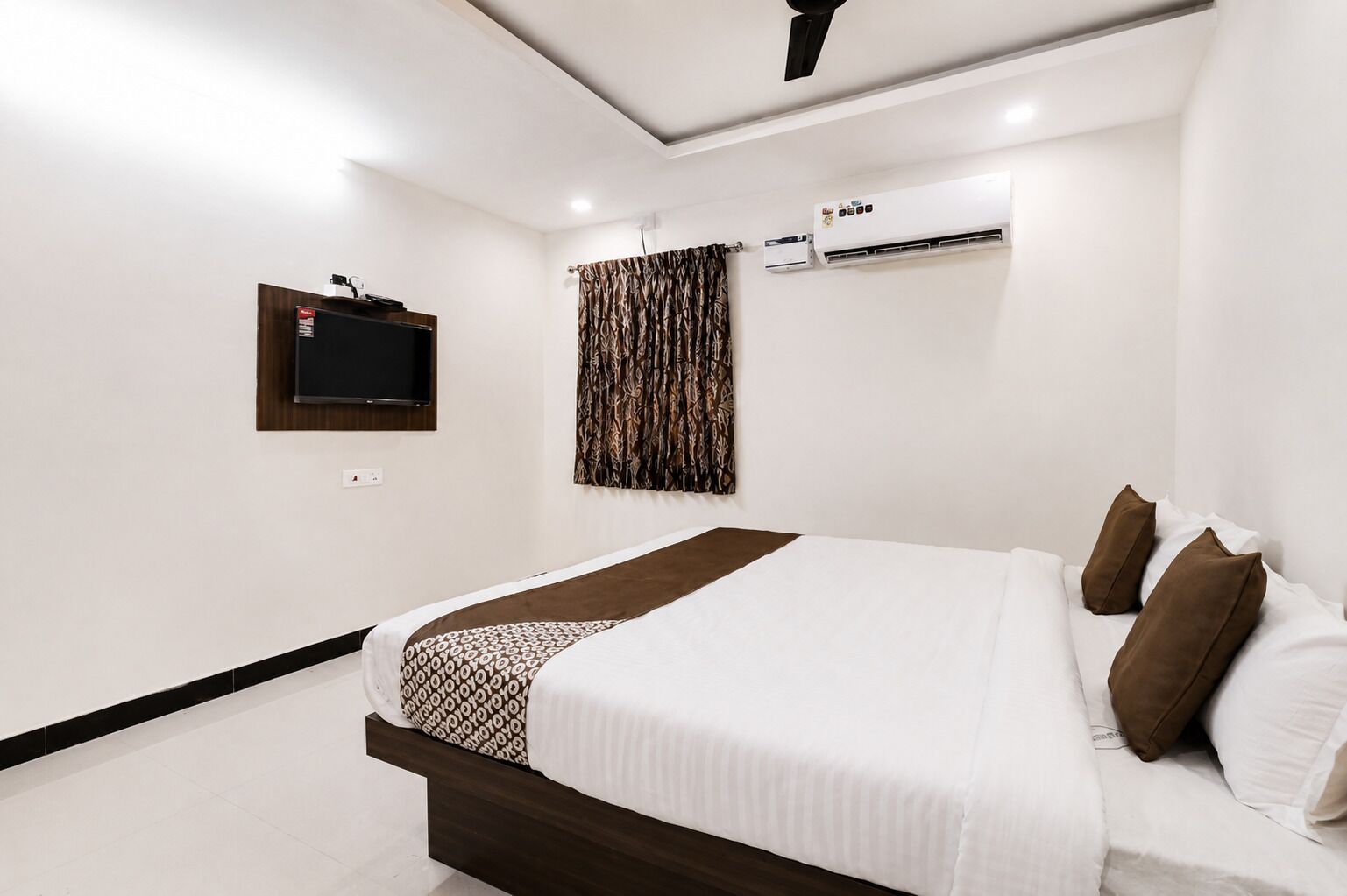 Een hotelkamer met een bed, een flatscreen televisie, een airconditioning en een plafondventilator.