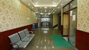 A hotel corridor with patterned wallpaper, metal chairs, a green mat, and a glass door with a sign. - JR Stays (Coimbatore)