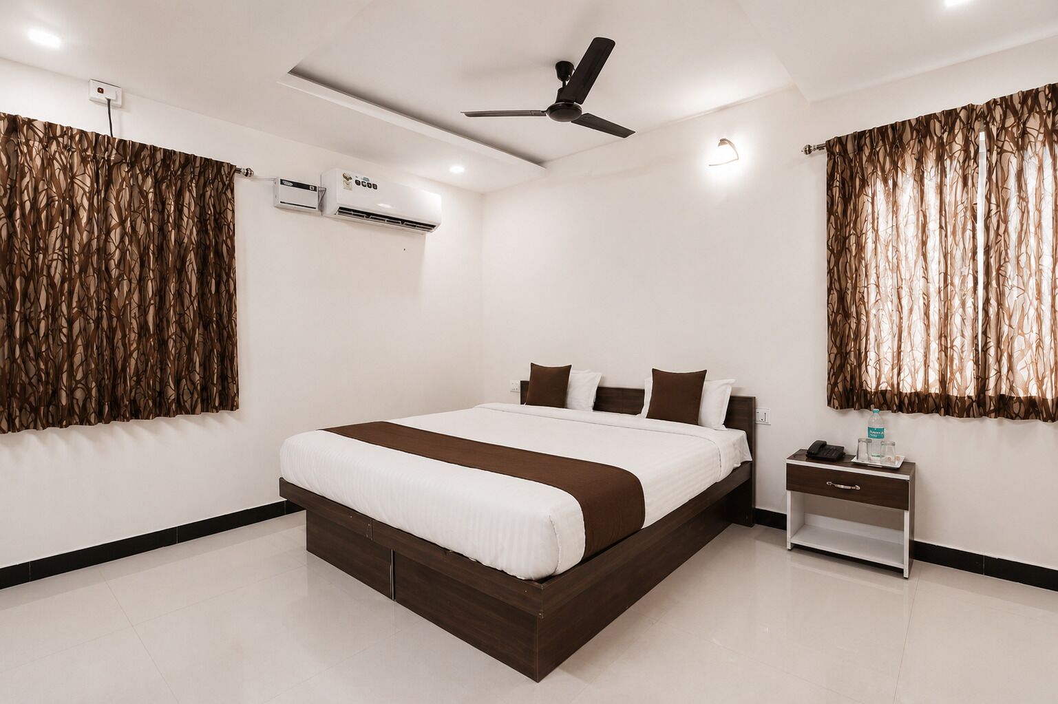 Una habitación de hotel moderna con una cama grande, una mesita de noche con lámpara, un aire acondicionado y un ventilador de techo.