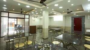 A spacious dining area with multiple tables and chairs, ceiling fans, and recessed lighting. - JR Stays (Coimbatore)