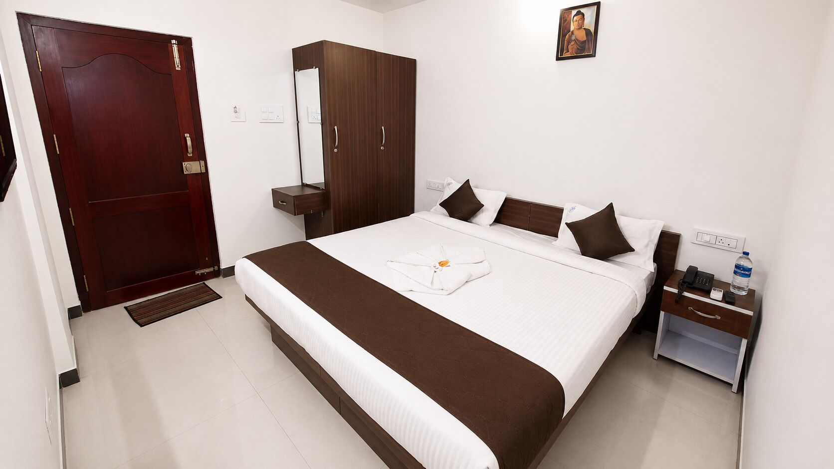 A hotel room with a bed, bedside table, wardrobe, and a door.