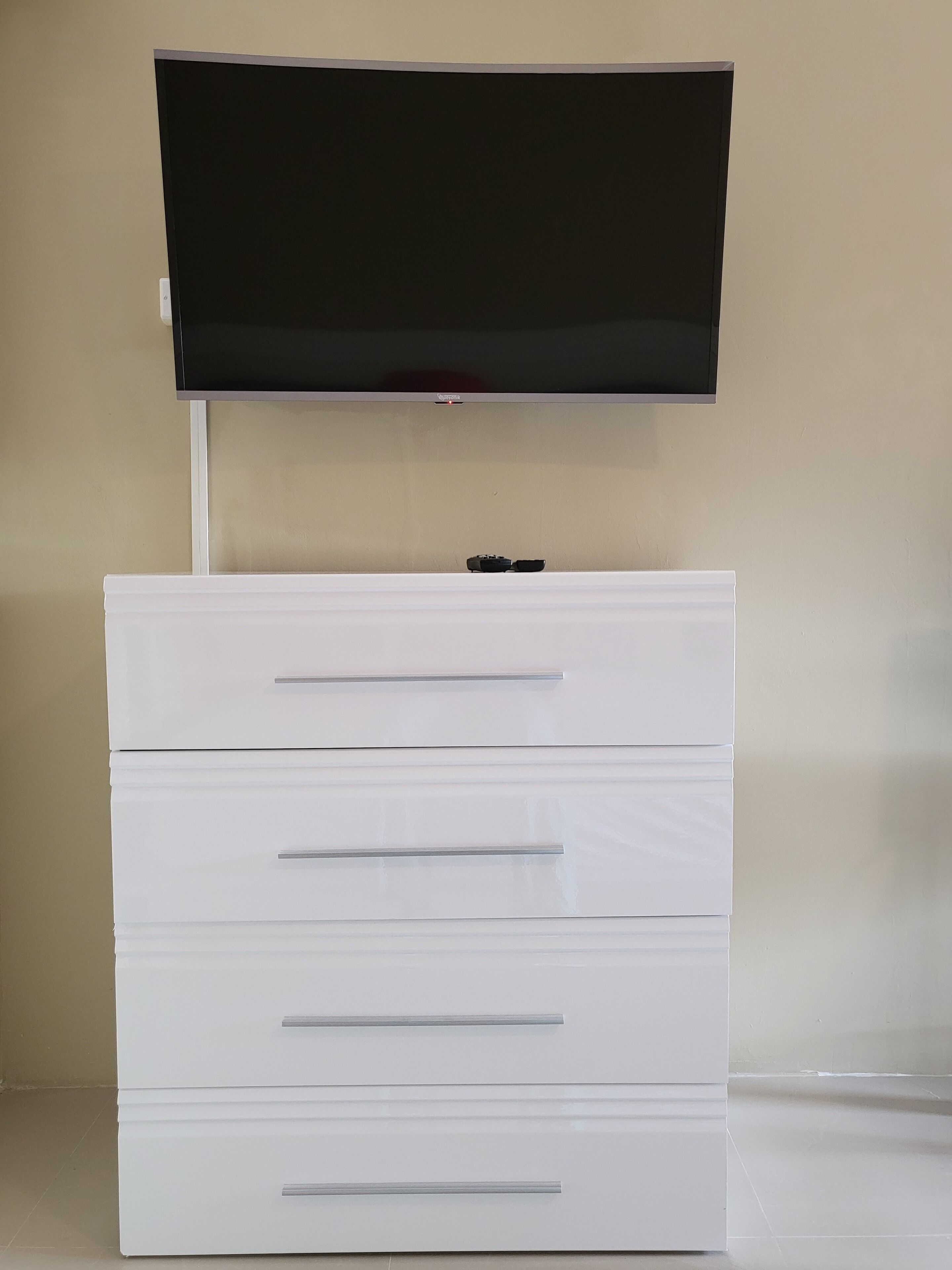 Un aparador blanc amb tres calaixos i un televisor de pantalla plana muntat a la part superior.