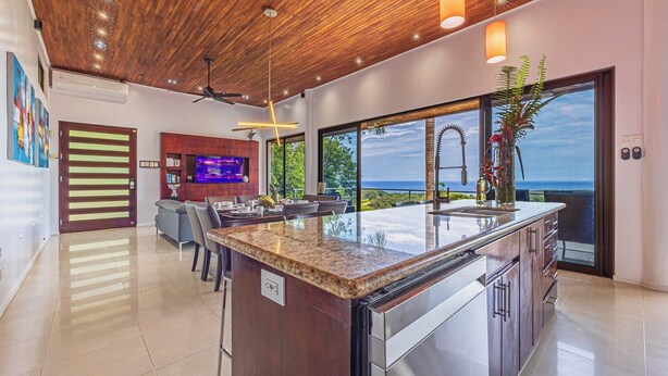 Une cuisine moderne dotée d’un grand îlot central, d’un coin repas avec télévision et d’une vue sur l’océan.