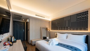 Een moderne hotelkamer met een groot bed, een bureau met stoel, een spiegel en een wand met decoratieve verlichting.