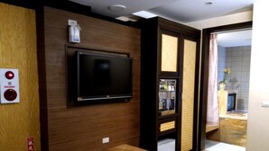 A hotel room with a flat-screen TV mounted on a wooden wall, a small seating area, a minibar, and a view of the bathroom through an open door. - Mapleton Motel (Taichung)
