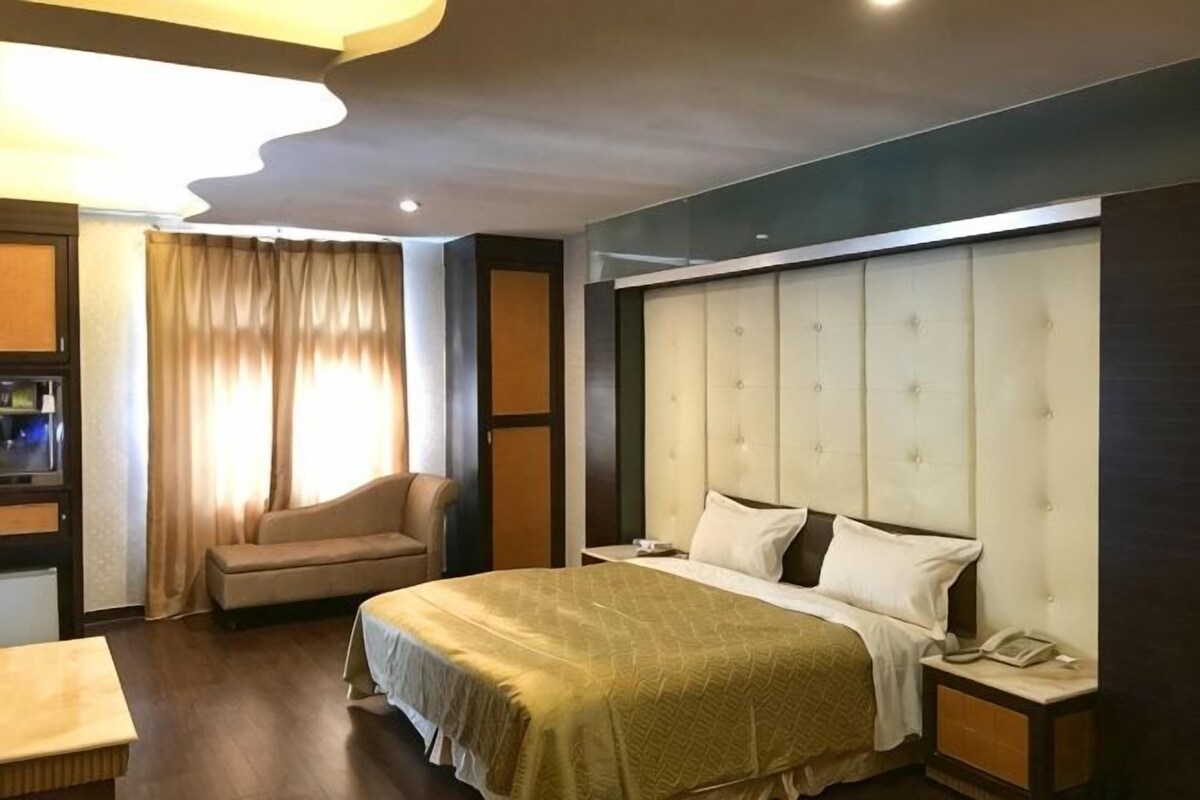 A hotel room with a large bed, a chair, a bedside table, and a TV.