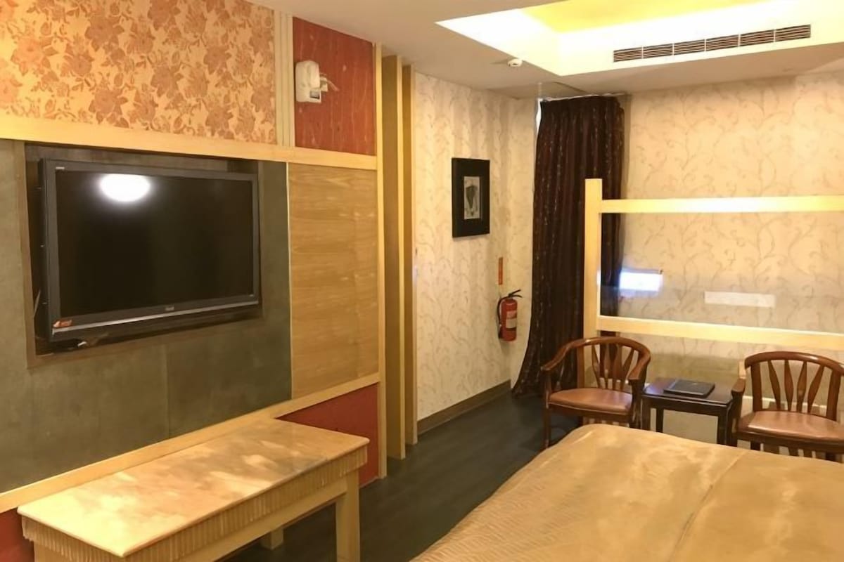 A hotel room with a bed, a TV, a bench, and a small table.
