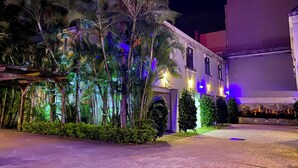 A hotel with a paved courtyard, palm trees, and illuminated exterior walls. - Mapleton Motel (Taichung)