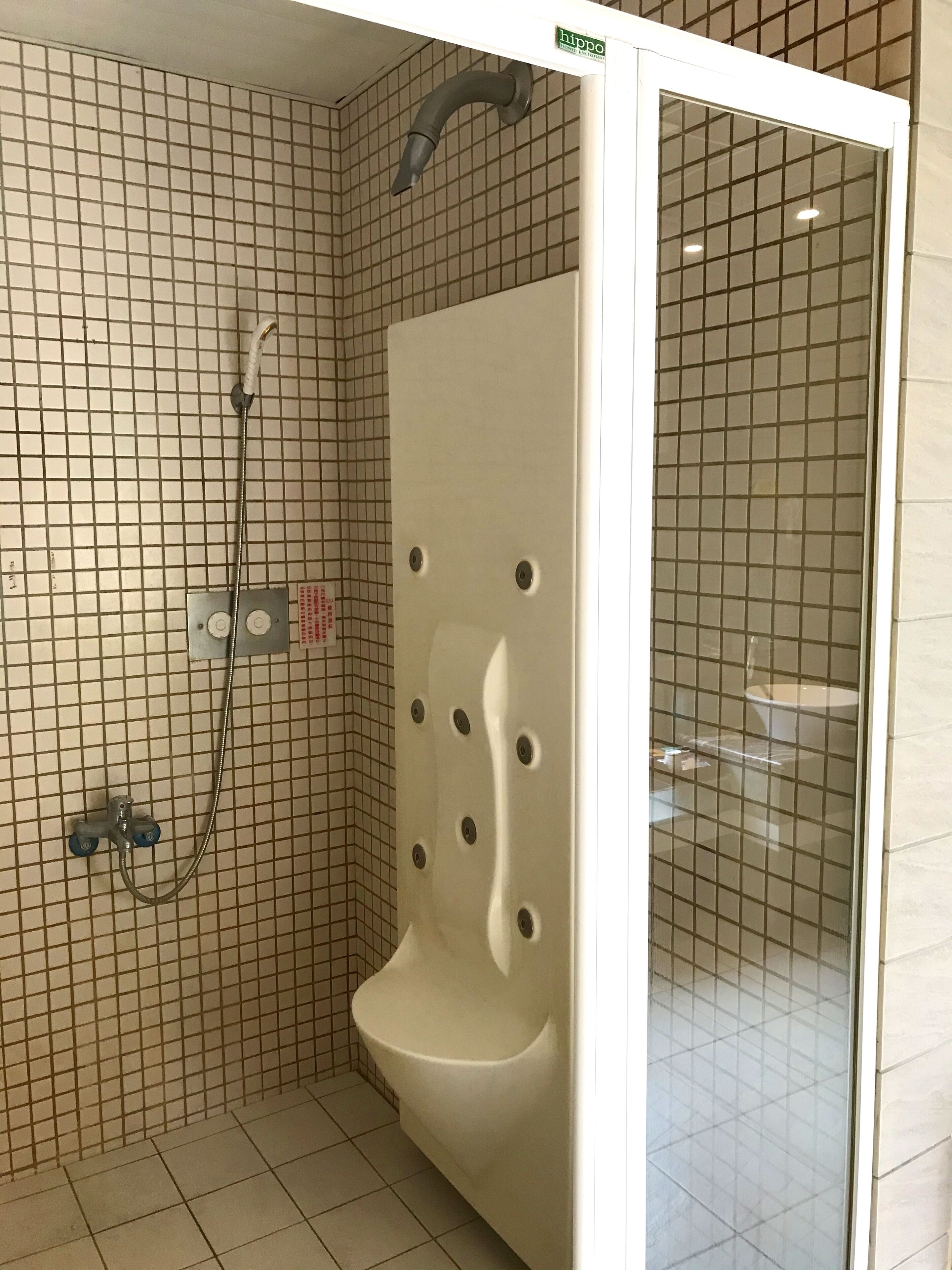 A bathroom with a tiled floor, a shower with a handheld showerhead, and a toilet.