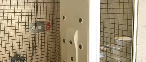 A bathroom with a tiled floor, a shower with a handheld showerhead, and a toilet.