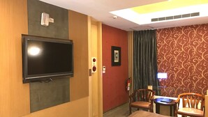 A hotel room with a flat-screen TV mounted on the wall, a fire extinguisher, a framed picture, and a patterned wallpaper. - Mapleton Motel (Taichung)