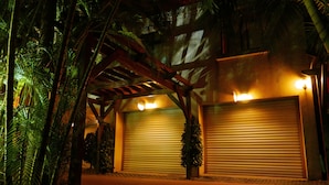 A building with two closed garage doors, surrounded by palm trees and a wooden pergola. - Mapleton Motel (Taichung)