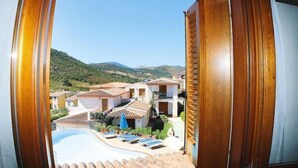 Vista de um resort com piscina, espreguiçadeiras e paisagem montanhosa ao fundo.