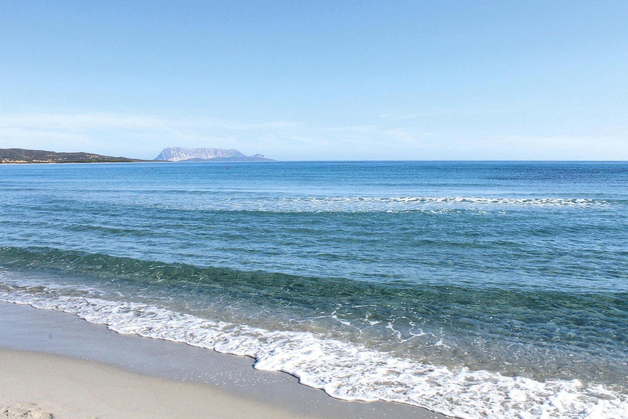 Een strand met helder water en een berg in de verte.
