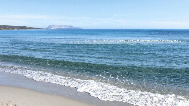 Una spiaggia con acque cristalline e una montagna in lontananza.