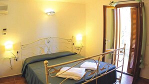 Una camera da letto con un letto con struttura in metallo, due abat-jour, un comodino e vista attraverso una porta con persiane in legno.
