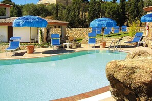 Une piscine entourée de murs de pierre et de verdure, avec des chaises longues bleues et des parasols.