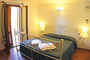 Un dormitorio con cama, lámparas de noche, ventana con persianas y una puerta.
