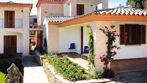 Un bâtiment à deux étages, doté d’un toit en tuiles, d’un balcon et d’un petit jardin agrémenté de plantes et d’un mur en pierre.