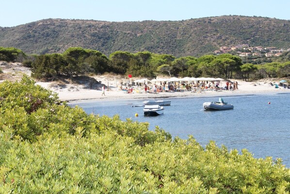 A beach with boats, a sandy shore, and a hill in the background.