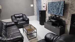 A living room with black leather sofas, a glass coffee table, a flat-screen TV, and a sound system. - Maddy's Den for females (Kolkata)