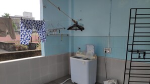 A small, tiled room with a window, a water dispenser, and a drying rack with clothes. - Maddy's Den for females (Kolkata)