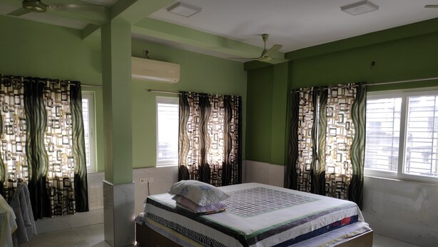 A bedroom with a bed, curtains, a ceiling fan, and a window. - Maddy's Den for females (Kolkata)