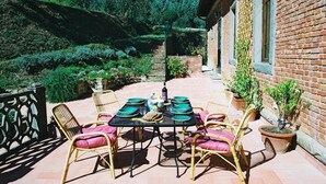 Eine möblierte Terrasse im Freien mit einem Esstisch, umgeben von Korbstühlen mit Kissen und Blumentöpfen.
