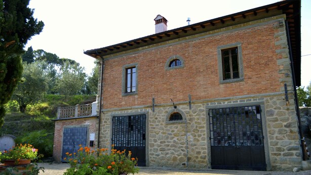 Ein zweistöckiges Steinhaus mit Ziegelverkleidung, zwei großen Metalltoren und einem kleinen Balkon.