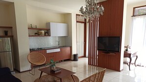 Uma sala de estar moderna com sofá, mesa de centro e televisão. Há uma área de cozinha com armários e fogão.