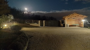 A wooden cabin with a bench and table, surrounded by a gravel path and a fence.